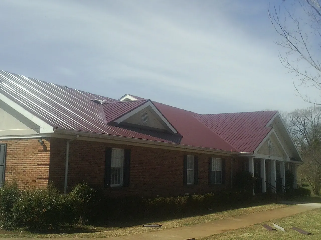 Red metal roof with gabled entries on a long brick building, from a Hail Damage Roof Repair job in Tucson